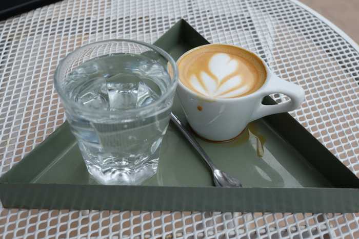 A macchiato with a side of sparkling water on a green triangular tray