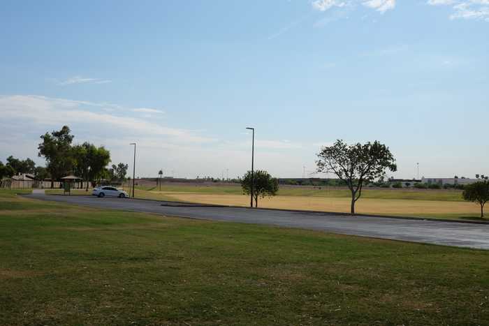 A big grass basin behind an almost empty parking lot to a park
