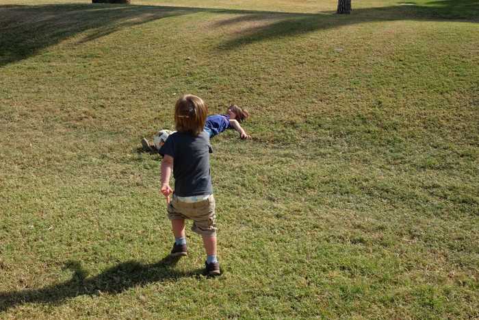 One kid running toward another kid laying down in some grass with a fall at their feet