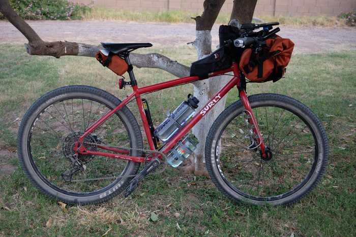 A Surly Bridge Club leaning on a tree with small saddle bag, pump, two bottles of water, top tube bag, feed bag, and large handlebar bag