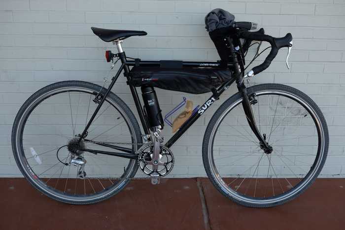 A black Surly Cross-Check with a klean kanteen in one bottle holder and a donut precariously sitting in the other