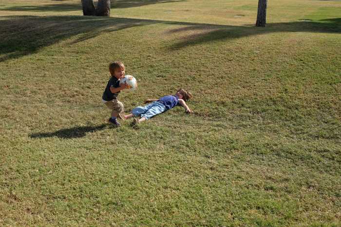 One kid with the ball in their hands turning to run away from the other kid laying in the grass