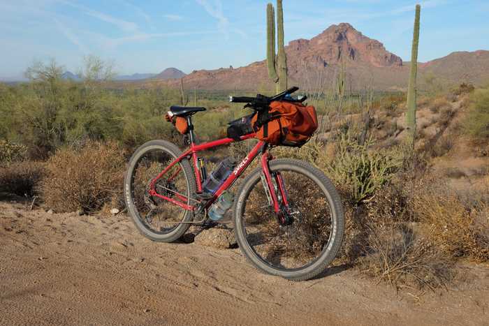 A red Surly Bridge Club on a dirt trail against a backdrop of cacti and Red Mountain
