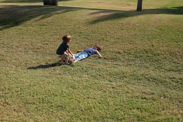 One kid bending over to pick up the soccer ball from the feet of the other kid