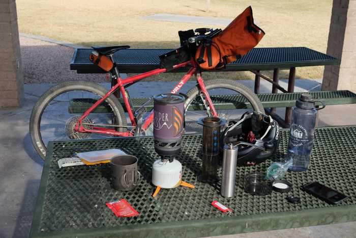A plethora of coffee and bike gear on a picnic table in a park