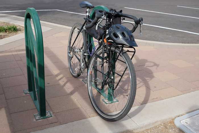 A Surly Cross-Check parked at a green bike rack with a black helmet sitting on its front rack
