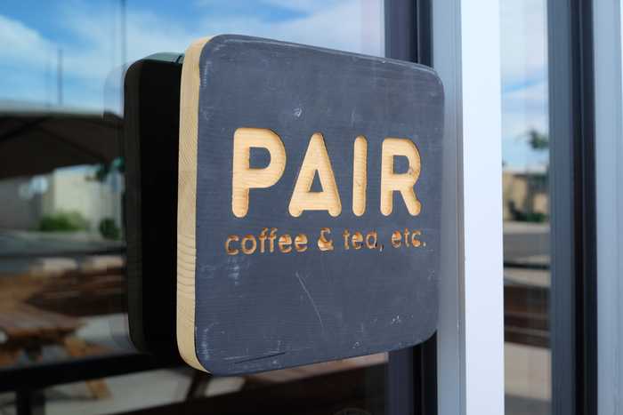 A wood sign on a glass window that says "PAIR coffee & tea, etc"