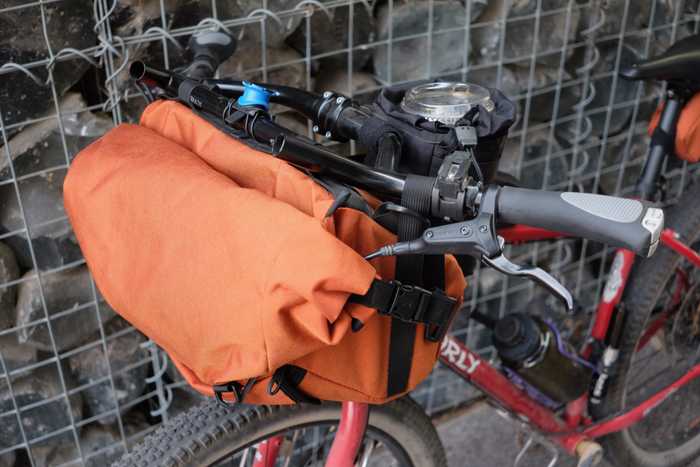 A close up of the front end of a Surly Bridge Club with a handlebar bag and a stem bag with a plastic coffee cup in it