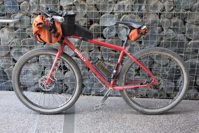 A red Surly Bridge Club in front of some decorative rocks with bags on the handlebars, stem, top tube, and saddle