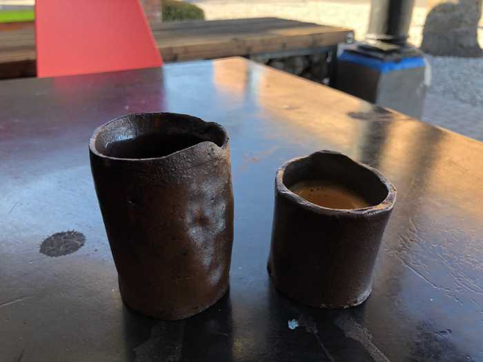 An espresso and sparkling water sitting on a table in homemade cups