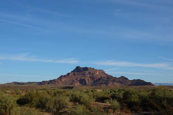 Red Mountain rising out of the desert against a blue sky with a few wispy white clouds